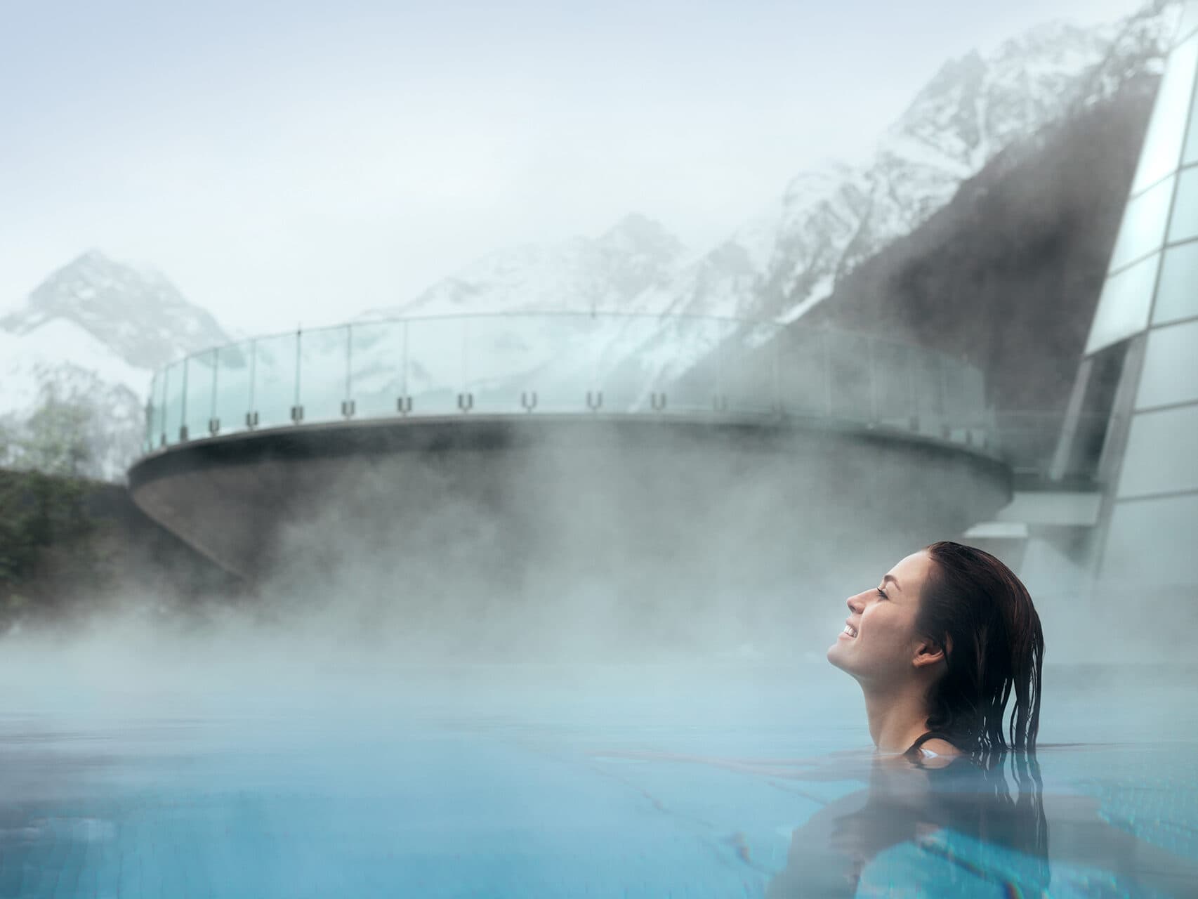 Inmitten einer verschneiten Berglandschaft genießt man die wohltuende Wärme eines Thermen-Außenbeckens, eingehüllt in dampfenden Dampf.