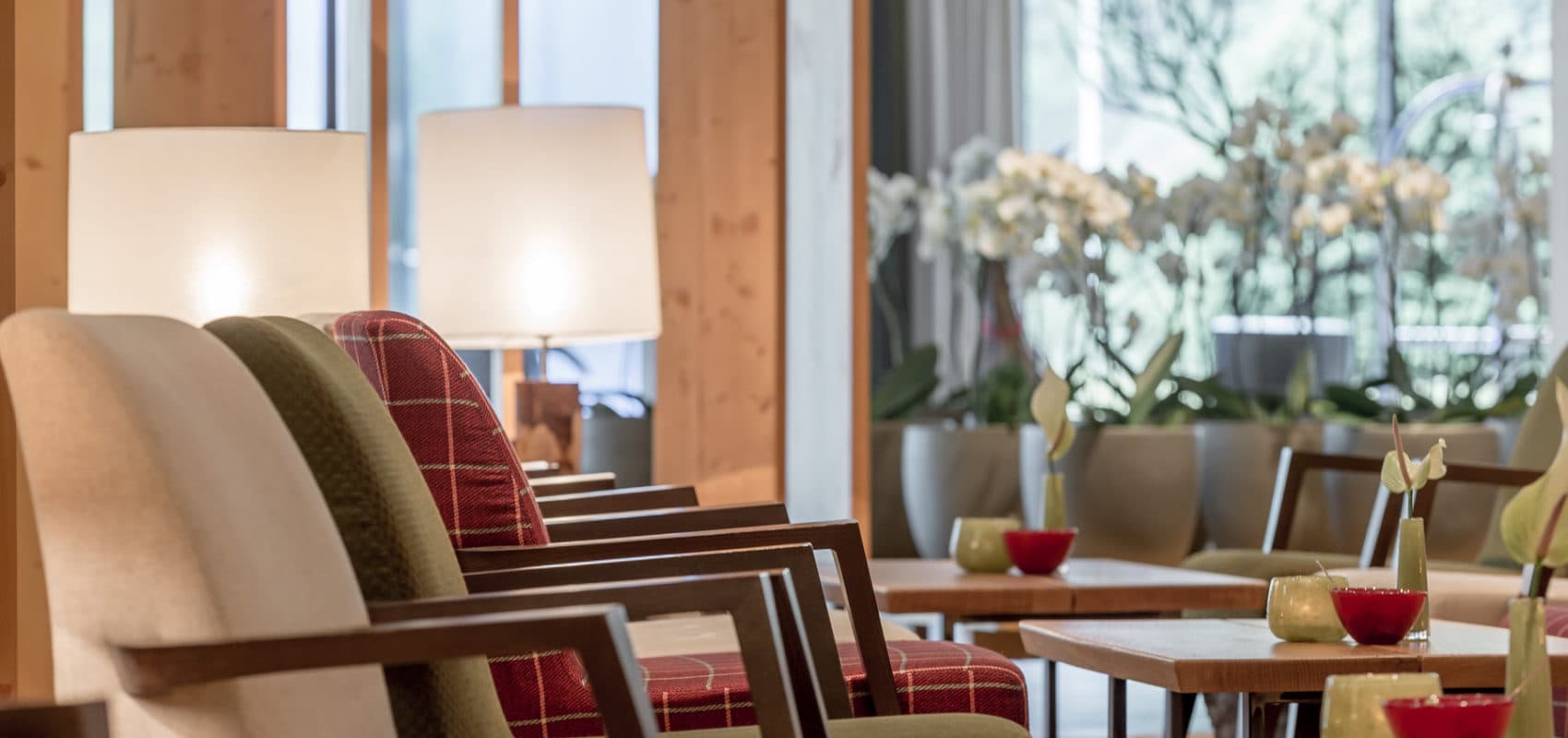 Chairs with varying patterns are arranged near tables with small decorative items. Large windows in the background provide natural light, casting a soft glow in the room.