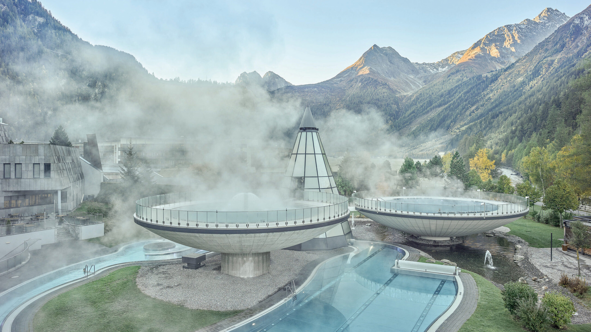 Ein geothermischer Spa-Komplex mit beeindruckenden dampfenden runden Becken und umgebenden Bergen vor einem klaren Himmel.