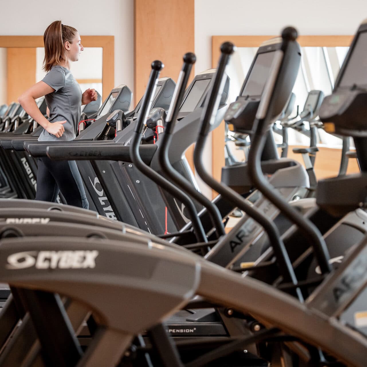Eine Frau konzentriert sich auf ihre Fitness, während sie in einem Fitnessstudio auf einem Laufband läuft, umgeben von mehreren unbesetzten Laufbändern.