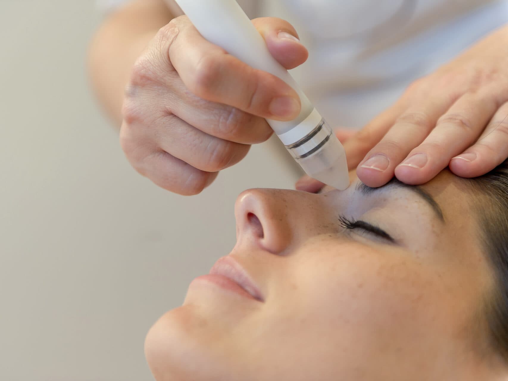 Nahaufnahme des Gesichts einer Person, die mit einem Handgerät auf der Stirn eine Hautpflegebehandlung erhält.