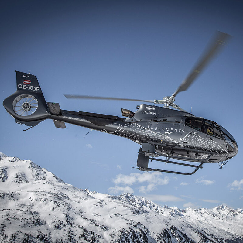 Ein Hubschrauber fliegt unter einem klaren blauen Himmel über schneebedeckte Berge.