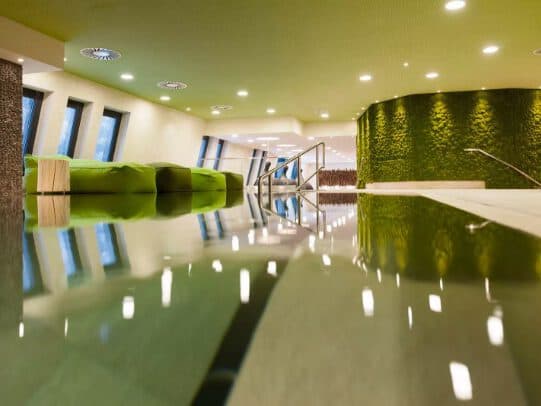 Modern interior with spa-like green accents, featuring a reflective floor, green wall, and curved seating area under circular ceiling lights.