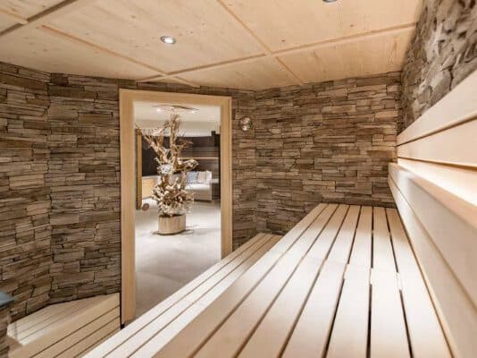 A serene wooden sauna with stone walls and benches invites relaxation, leading to a spa room adorned with a unique wooden sculpture.