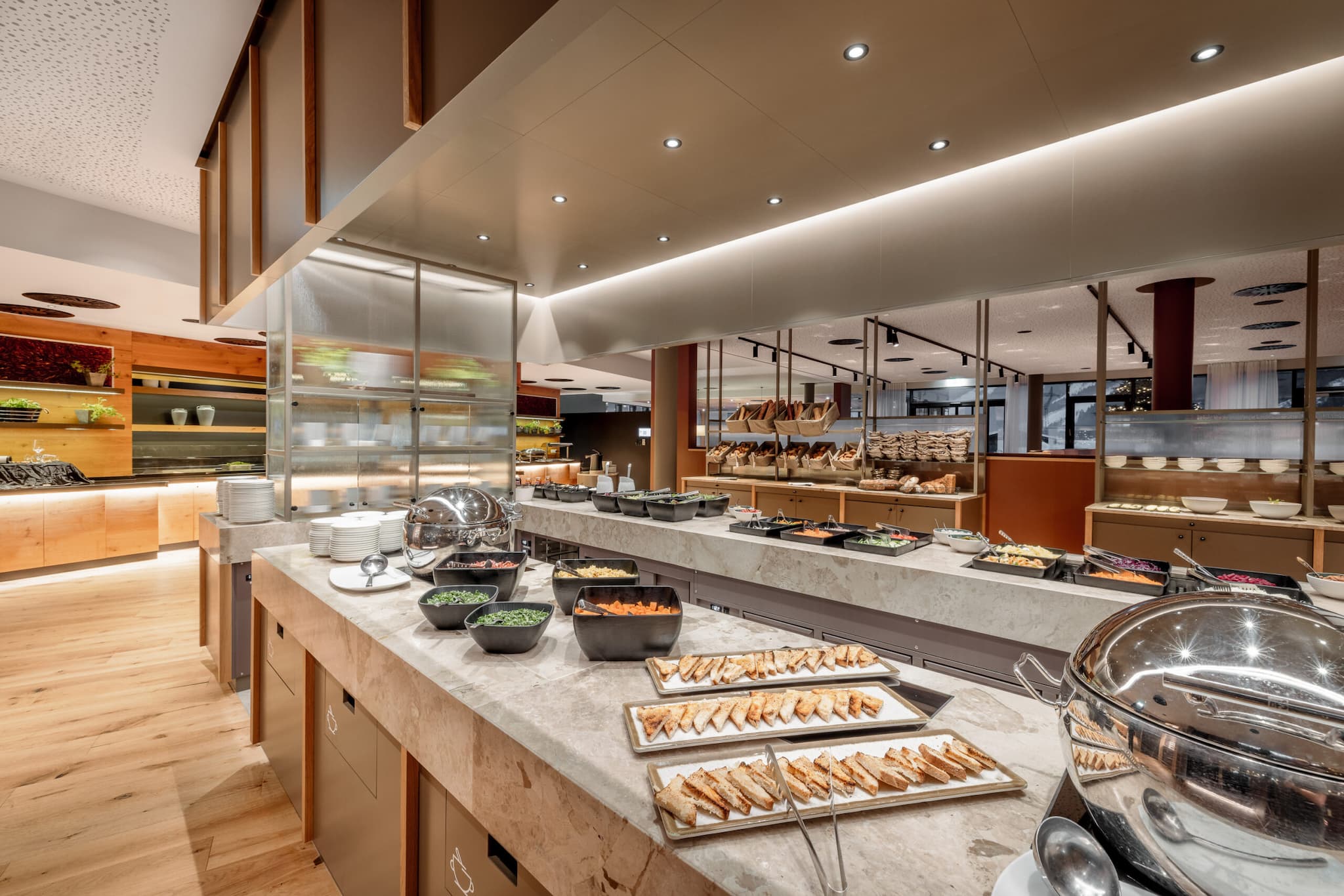 A buffet restaurant with a variety of dishes showcased on a marble countertop. Shelves, bowls, and trays are set in a spacious, well-lit environment with wood and metal accents. Perfect for those exploring standout restaurants.