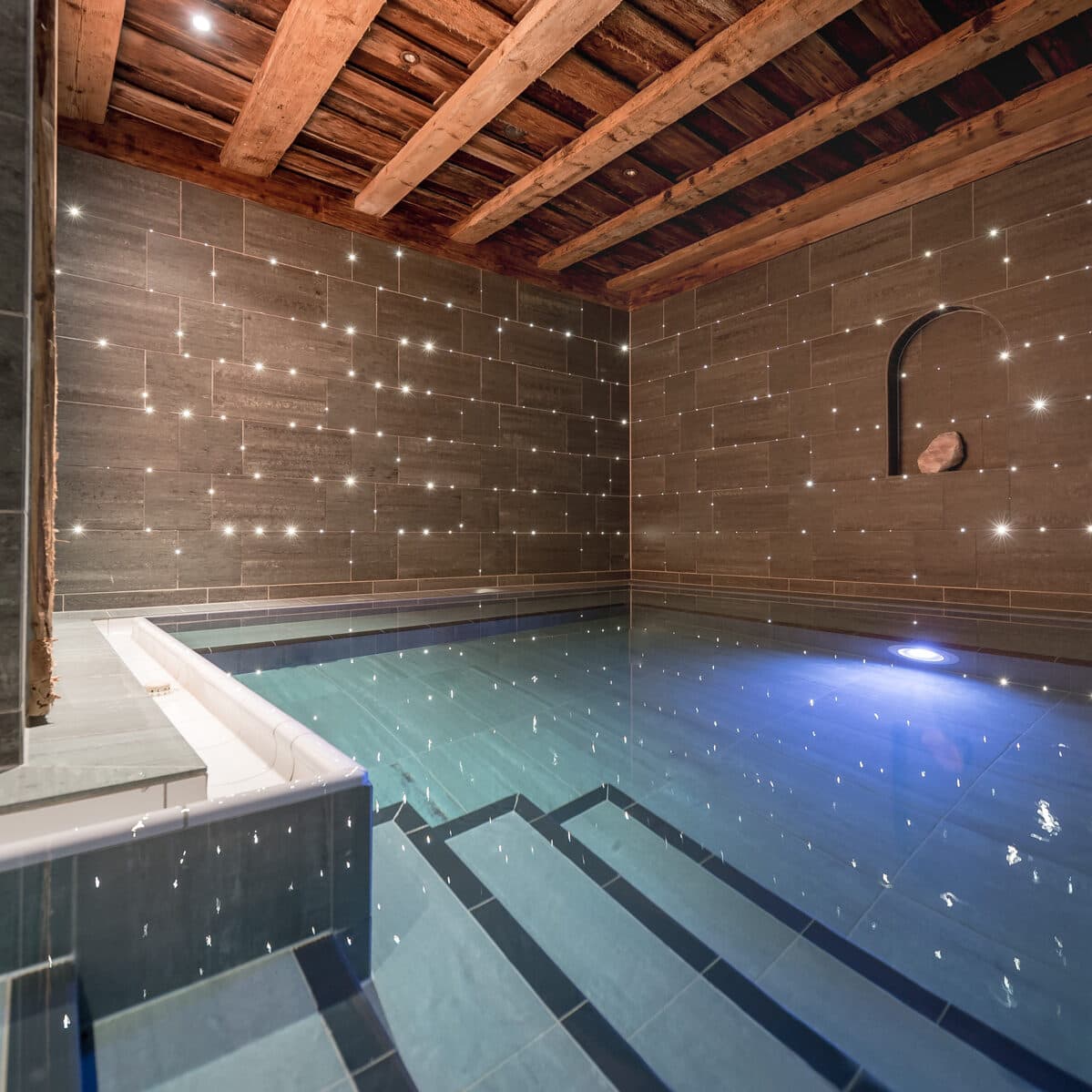 Innenpool mit gefliesten Wänden, Holzdecke, Unterwassertreppe und kleinen, in die Wände eingelassenen Lichtern, die einen sternförmigen Effekt erzeugen.