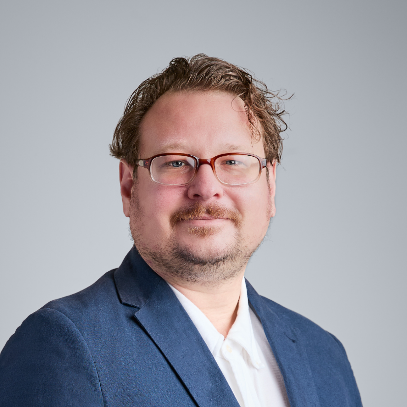 Porträtfoto eines Mannes mit Brille und blauem Blazer.